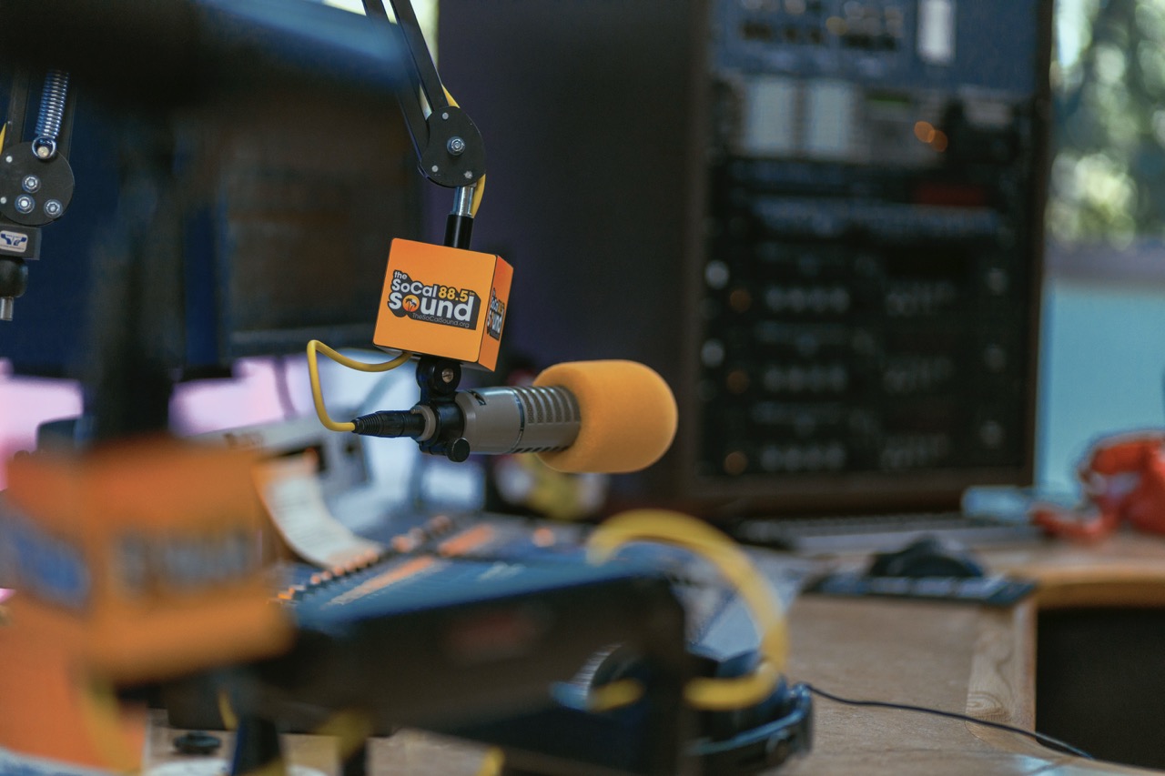On-air studio console with microphone flag and other microphone in foreground